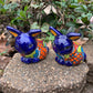 Two colorful Mexican Talavera rabbit figurines on a stone surface with greenery in the background set of two azul