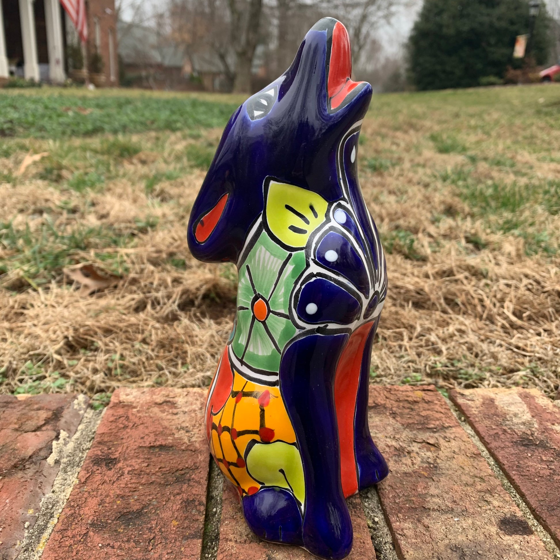 Colorful Talavera Coyote figure on a brick surface with a grassy area in the background