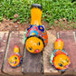 Three hand-painted ceramic bird figurines in yellow, orange  blue, red, and black, displayed on a brick surface with a green grass background top view