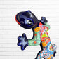 A colorful Mexican Talavera wall sculpture of a lizard, featuring a vibrant multicolor pattern with dark blue, orange, red, green, and yellow, mounted on a white brick wall, close-up of face and eyes.