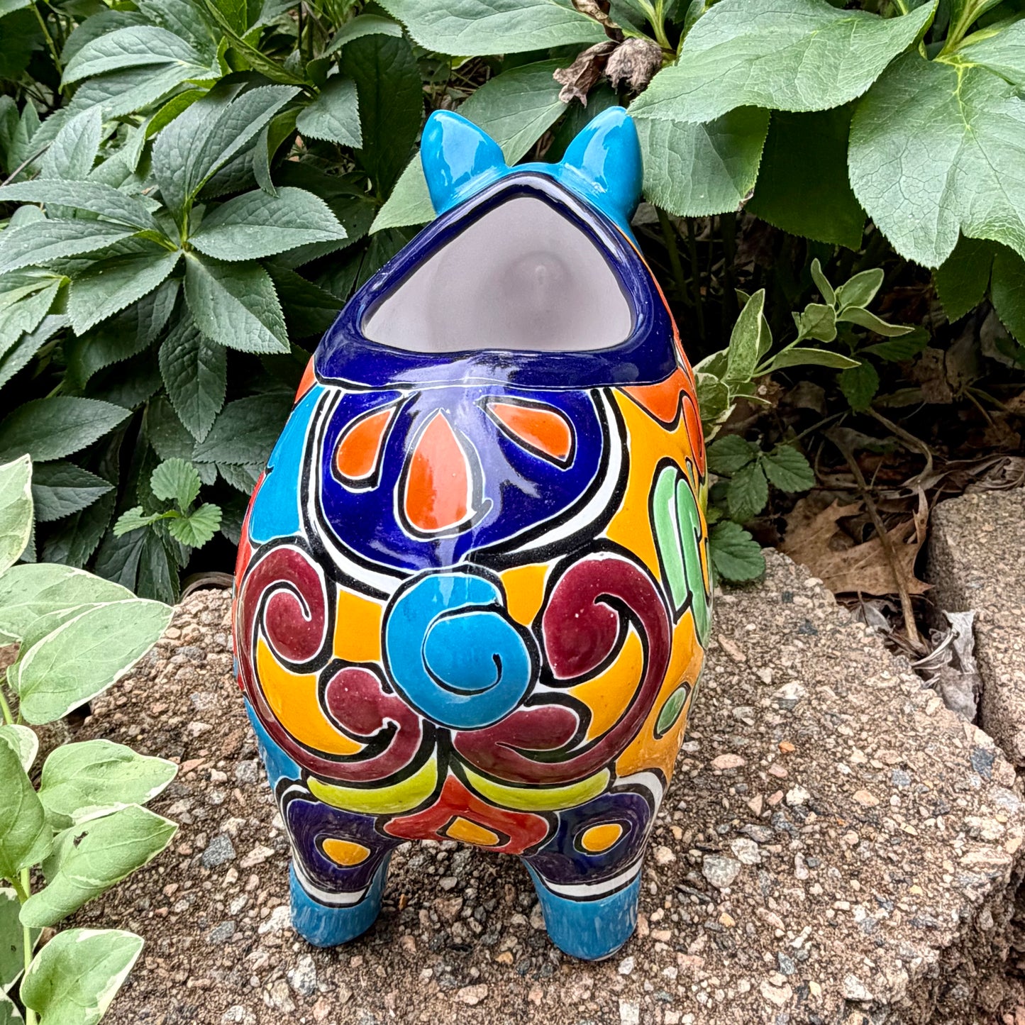 Colorful Talavera ceramic pig planter on a stone surface with green plants in  Background back view