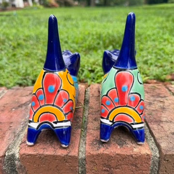 Two cobalt blue with multi-color designs hand-painted talavera ceramic cat figurines resting on a brick ledge with a green grassy lawn back tail view.