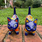 Two colorful hand-painted talavera ceramic cat figurines in cobalt blue with multi color designs standing on a brick path with a green lawn front face view.