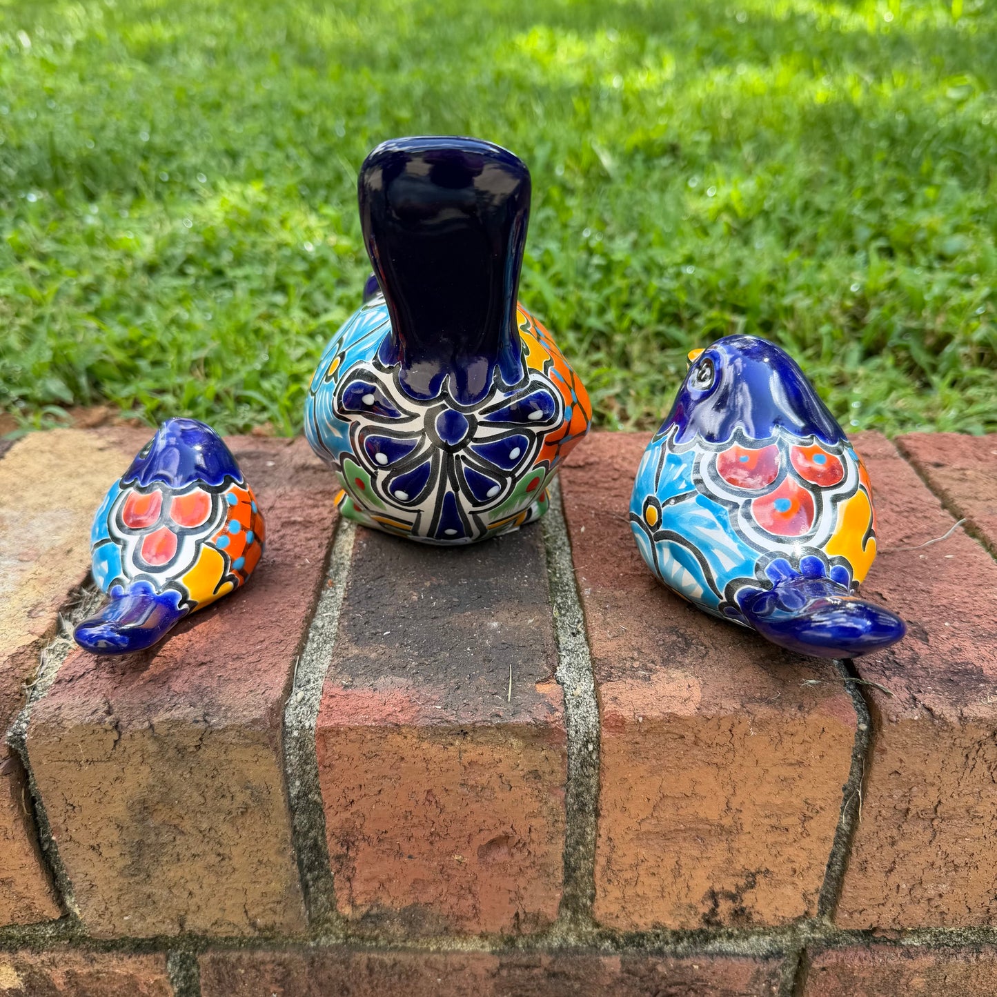 Three hand-painted ceramic bird figurines in different sizes, decorated with a vibrant Mexican Talavera style pattern of blue, red, yellow, and white showing back view.
