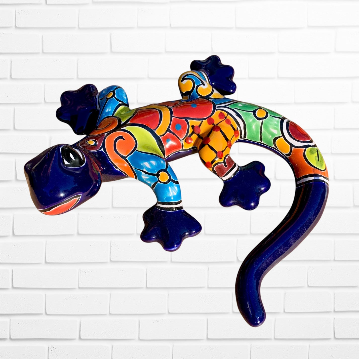 Colorful lizard-shaped wall art against a white brick wall background side