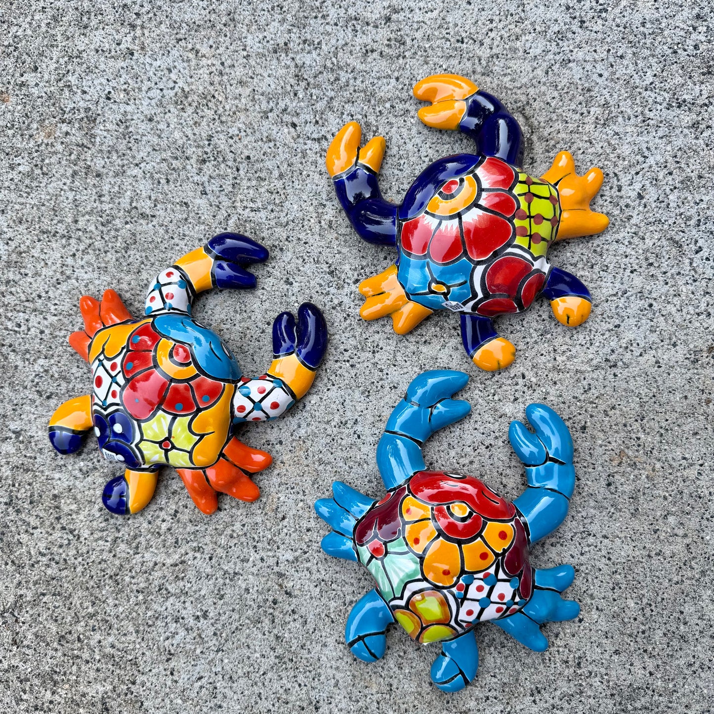 Three colorful hand-painted Talavera ceramic crabs arranged on a textured gray concrete surface.
