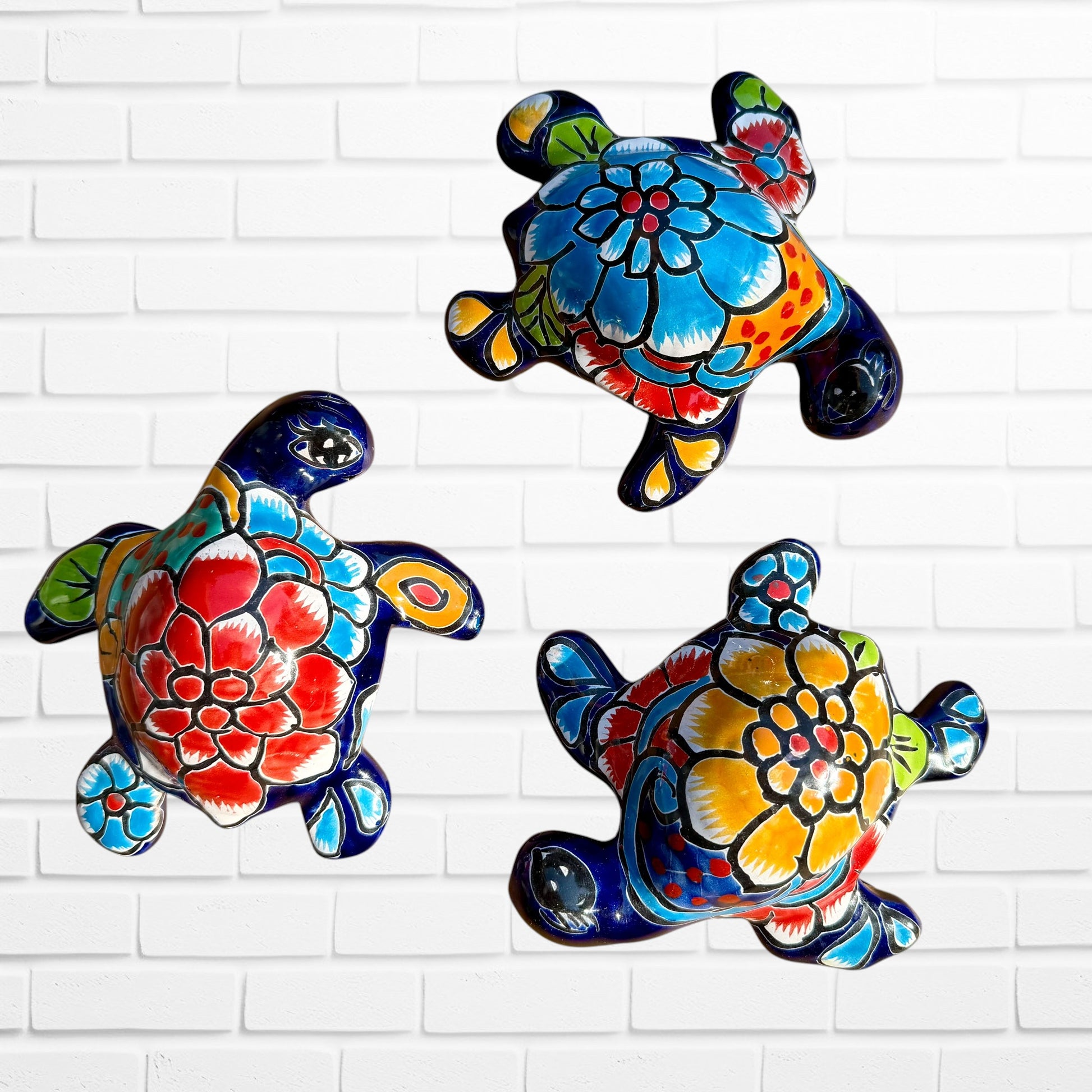 Three colorful hand-painted ceramic sea turtle wall art pieces displayed against a white painted brick wall.