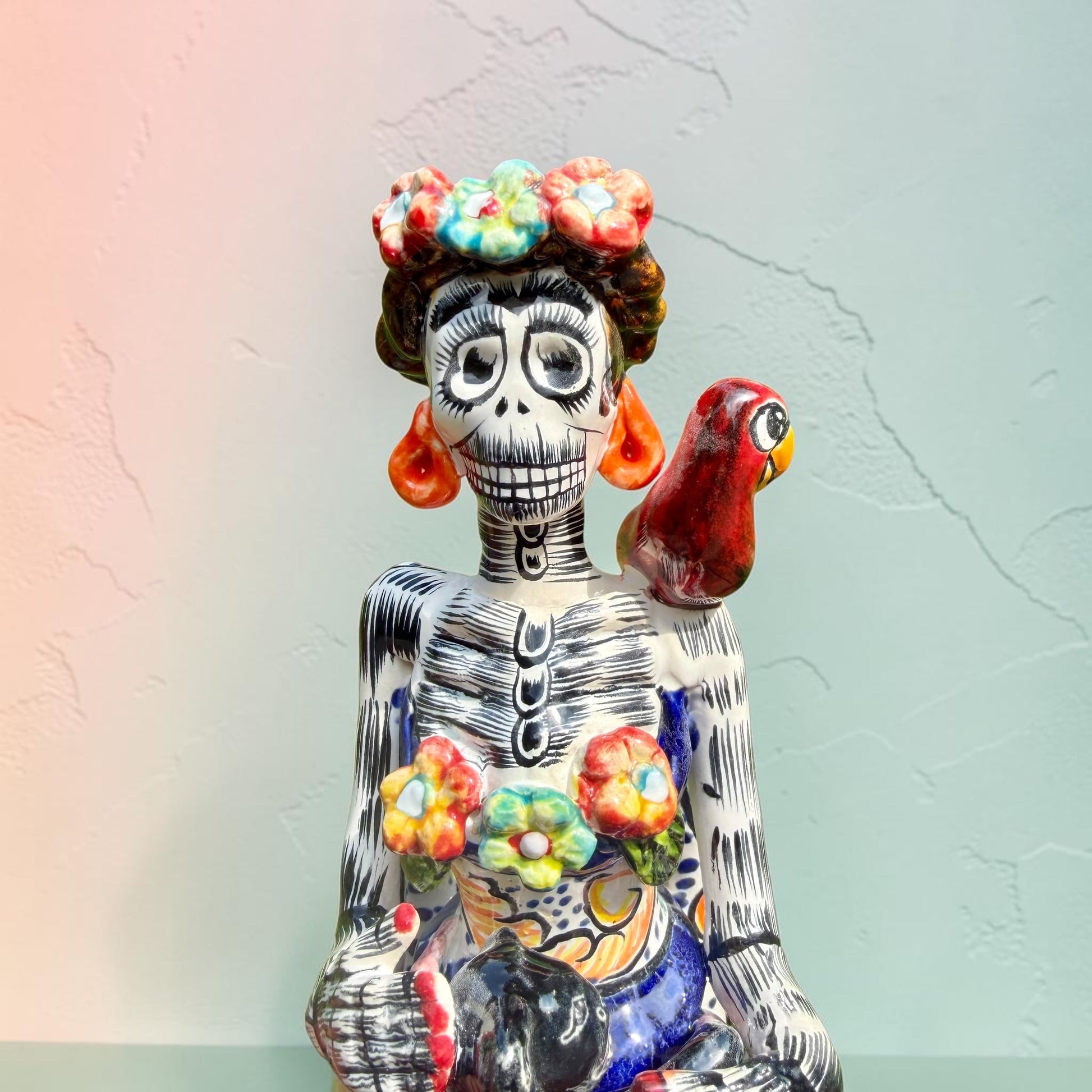 Frida Kahlo Talavera day of the dead figurine sitting in a chair holding a monkey with a parrot on her shoulder, close up of her face. 