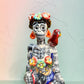 Frida Kahlo Talavera day of the dead figurine sitting in a chair holding a monkey with a parrot on her shoulder, close up of her face. 
