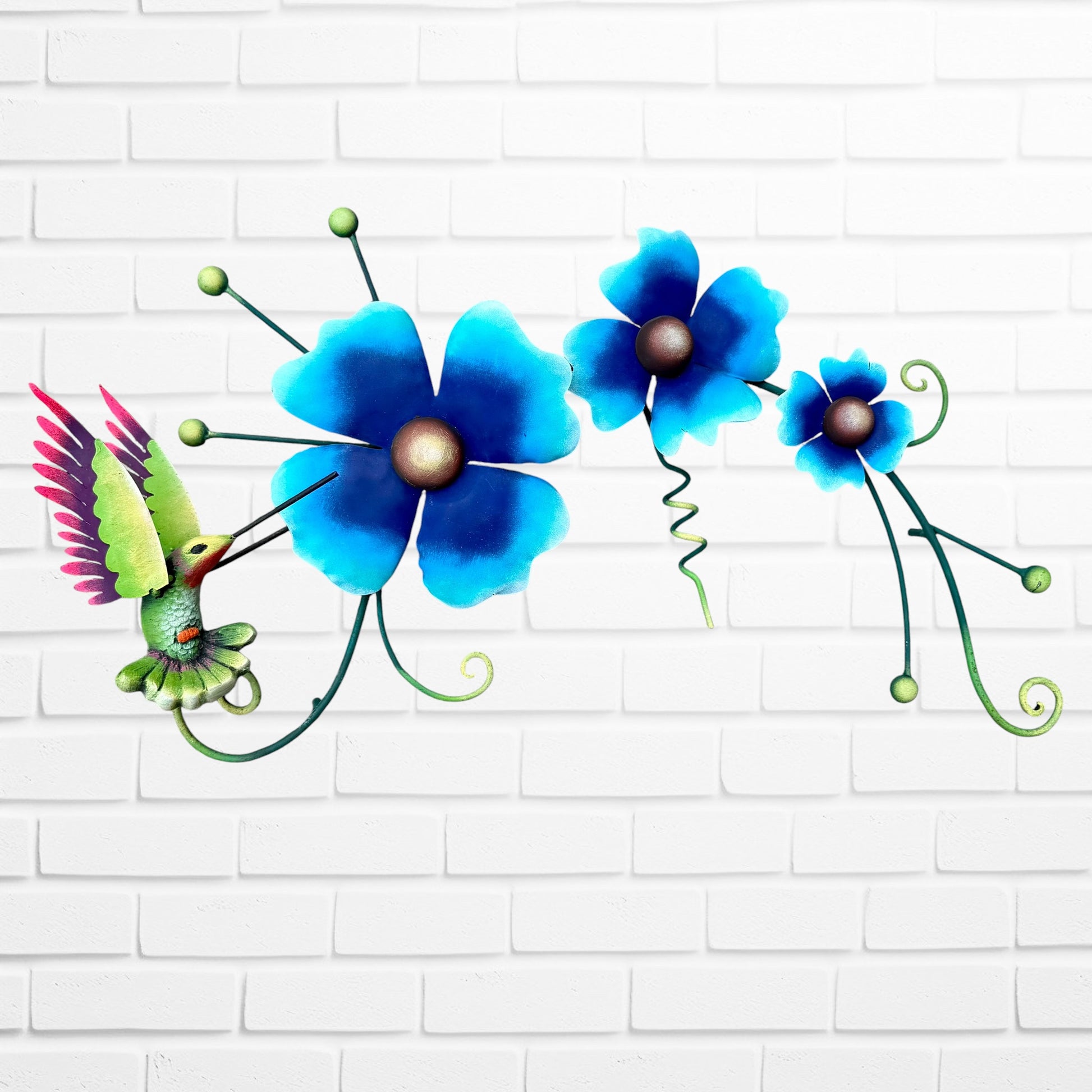 Decorative metal wall art with three blue flowers and a colorful hummingbird on a white brick background full front view