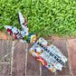 A hand-painted Mexican Talavera-style donkey figurine with a skeletal design, standing on a colorful floral base outdoors on a brick path with a green lawn in the background. Top view of donkey, Showing the backbone.