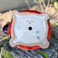 A colorful talavera turtle planter with a hand-painted Mexican-style pattern in orange, blue, yellow, and white, sitting on a mossy stone outdoors. Bottom drain hole.