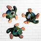 Three colorful hand-painted talavera ceramic sea turtles with floral patterns on their shells, displayed against a white brick wall background, back view.