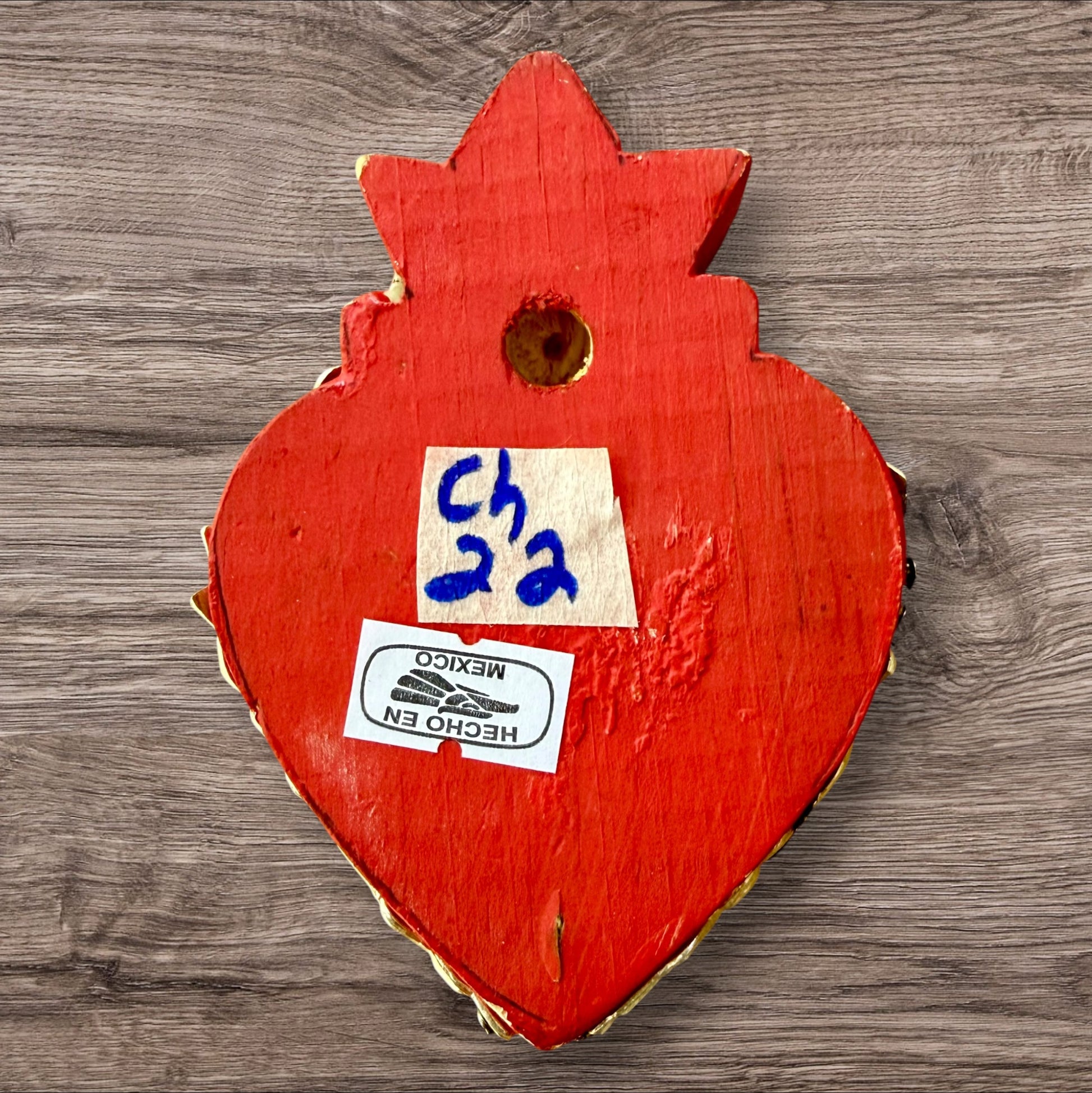 A Mexican Milagros heart in red with a gold flaming top, covered in silver charms, back view.