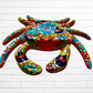 A colorful multicolor hand-painted wall art sculpture of a crab, decorated with vibrant floral patterns, shown against a white brick wall background, front face.