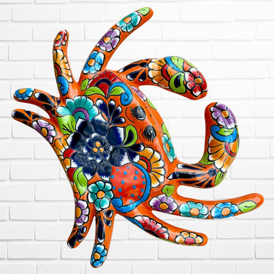 Colorful hand-painted Talavera wall art sculpture of a crab, decorated with intricate floral and folk-art patterns in orange, blue, green, purple, and red, mounted on a white brick wall.