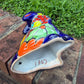A colorful hand-painted talavera ceramic coyote figurine sitting on a brick surface with a blurred green lawn and trees in the background bottom view