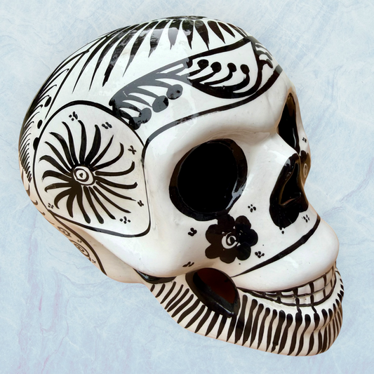 A decorative skull sculpture with intricate black sugar skull style patterns painted on an off-white base, set against a light blue textured background.
