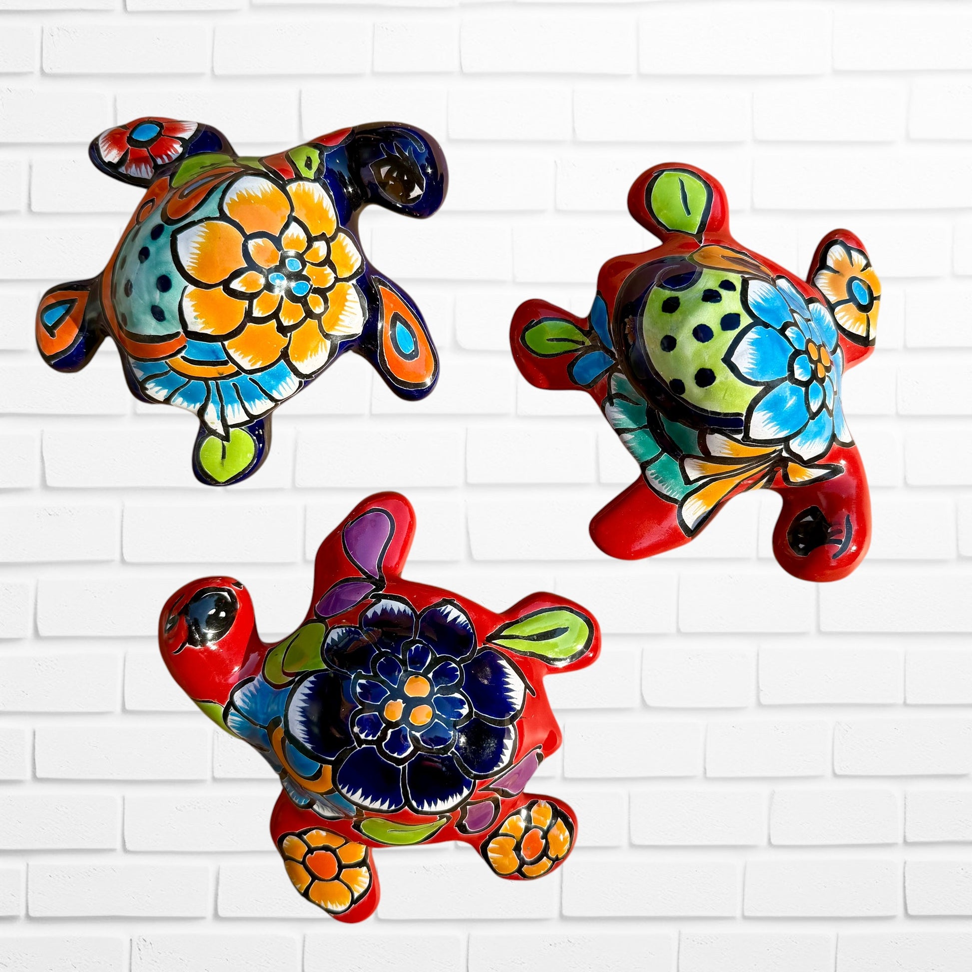 Three colorful hand-painted Mexican Talavera sea turtle wall art pieces with floral patterns, displayed on a white brick wall.