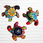 Three colorful hand-painted Mexican Talavera sea turtle wall art pieces with floral patterns, displayed on a white brick wall.