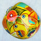 A vibrant yellow sugar skull decorated with colorful floral and geometric patterns in blue, red, black, and white, set against a light blue textured background, top view of skull.