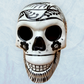 A decorative skull sculpture with intricate black sugar skull style patterns painted on an off-white base, set against a light blue textured background, front view.