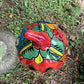 A hand-painted talavera halloween  jack-o'-lantern candle holder in red, green, black, and orange, displayed on a stone pedestal in an outdoor garden setting top of pumpkin view.