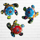 Three colorful hand-painted talavera ceramic sea turtles with floral patterns on their shells, displayed against a white brick wall background.