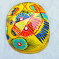 A vibrant yellow sugar skull decorated with colorful floral and geometric patterns in blue, red, black, and white, set against a light blue textured background, back view of skull.