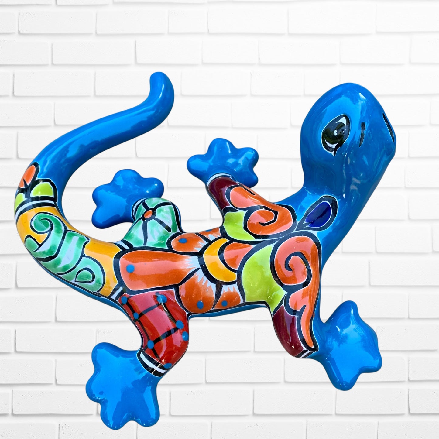 Colorful lizard-shaped wall art against a white brick wall background left side