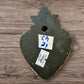 A Mexican Milagros heart in black with a gold flaming top, covered in silver charms, back of heart view. 