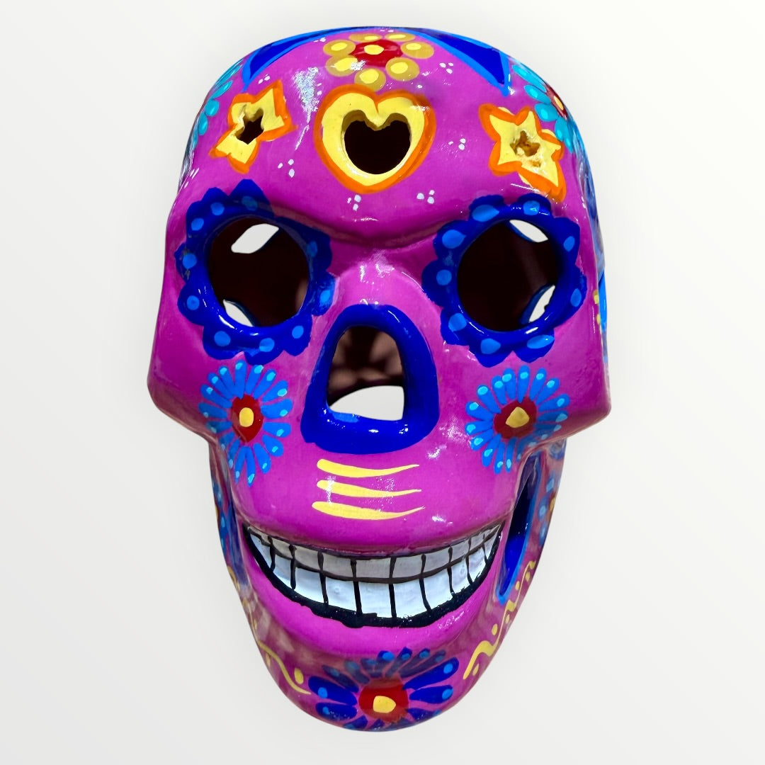 A hand-painted ceramic sugar skull mask in vibrant magenta pink, decorated with colorful floral and geometric patterns in blue, yellow, red, and white, set against a plain white background Front face view.