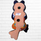 A colorful ceramic frog figurine sitting with arms crossed, decorated with vibrant hand-painted patterns in blue, yellow, red, orange, and light blue, set back view with hanging holes. 