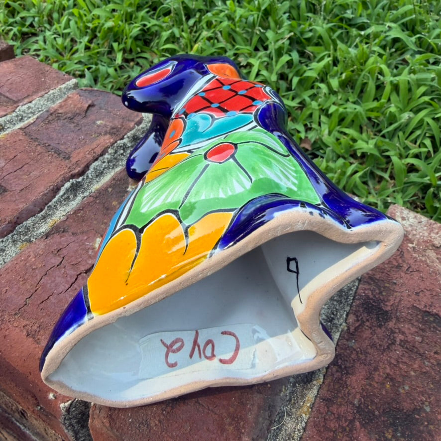 A colorful hand-painted Mexican Talavera Ceramic dog figurine sitting on a brick wall with a green grassy lawn and a house in the background bottom.