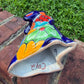 A colorful hand-painted Mexican Talavera Ceramic dog figurine sitting on a brick wall with a green grassy lawn and a house in the background bottom.