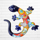 A colorful Talavera ceramic wall sculpture of a salamander, featuring a glossy finish and intricate hand-painted patterns in blue, orange, red, yellow, and white, mounted against a white brick wall, front body view.