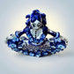 A Day of the Dead style talavera figurine of a skeleton woman in a wide floral skirt, painted in deep blue, black, white, and light blue on a soft beige-to-blue gradient background. Top view of ballerina figurine.