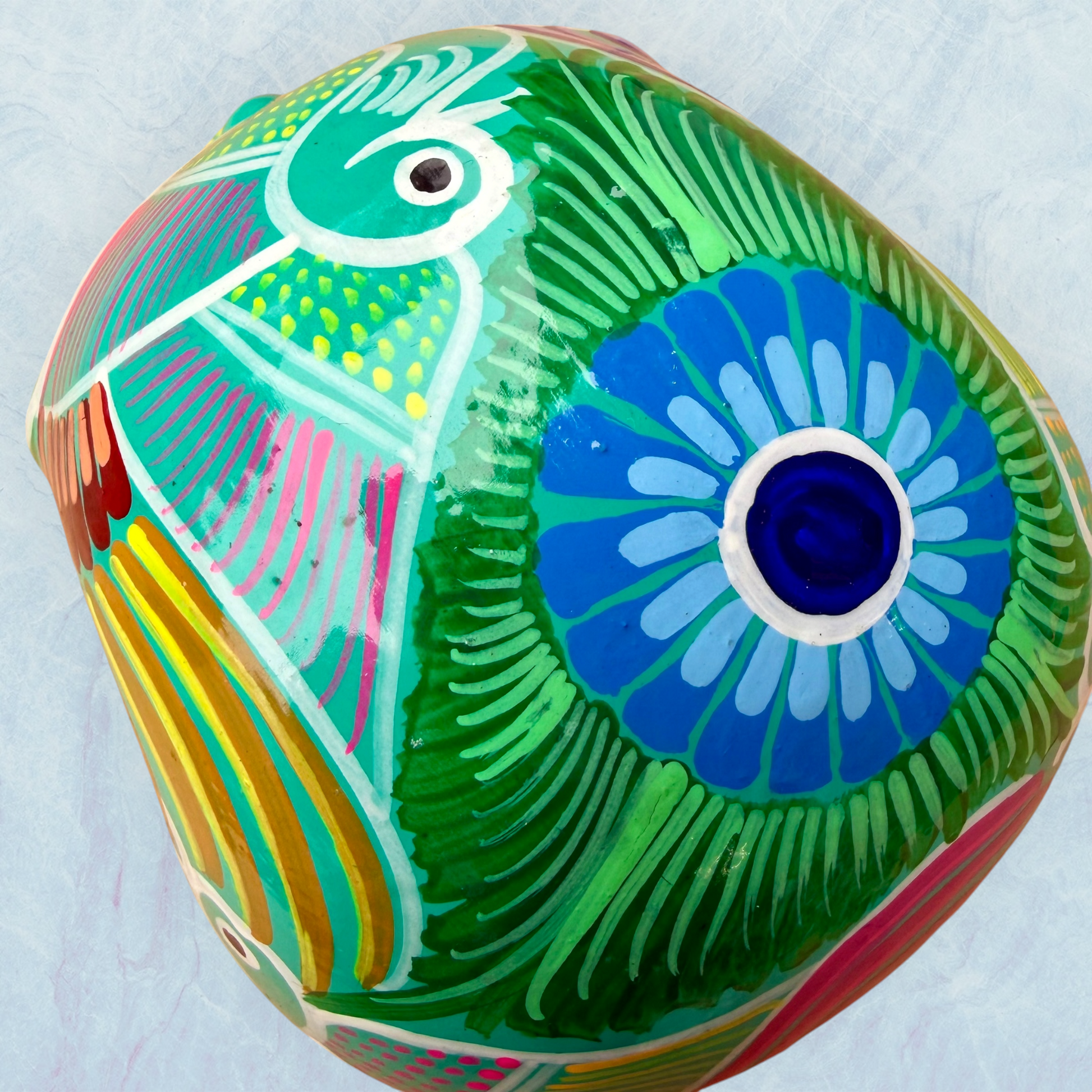 A decorative skull sculpture with intricate colorful sugar skull style patterns painted on a teal colored base, set against a light blue textured background, top view.