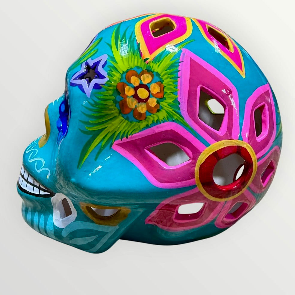 A decorative sugar skull painted in bright turquoise blue with colorful floral and geometric patterns in pink, yellow, green, purple, and white, shown against a plain light background side view