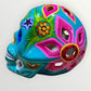 A decorative sugar skull painted in bright turquoise blue with colorful floral and geometric patterns in pink, yellow, green, purple, and white, shown against a plain light background side view