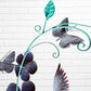 Decorative metal wall art with butterfly, hummingbird  and  flowers with  leaf design against a white brick wall back view hanging loop