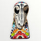 A ceramic Mexican-style skeleton dog figurine standing on a colorful floral base against a plain white background. Front face close up of catrina dog.