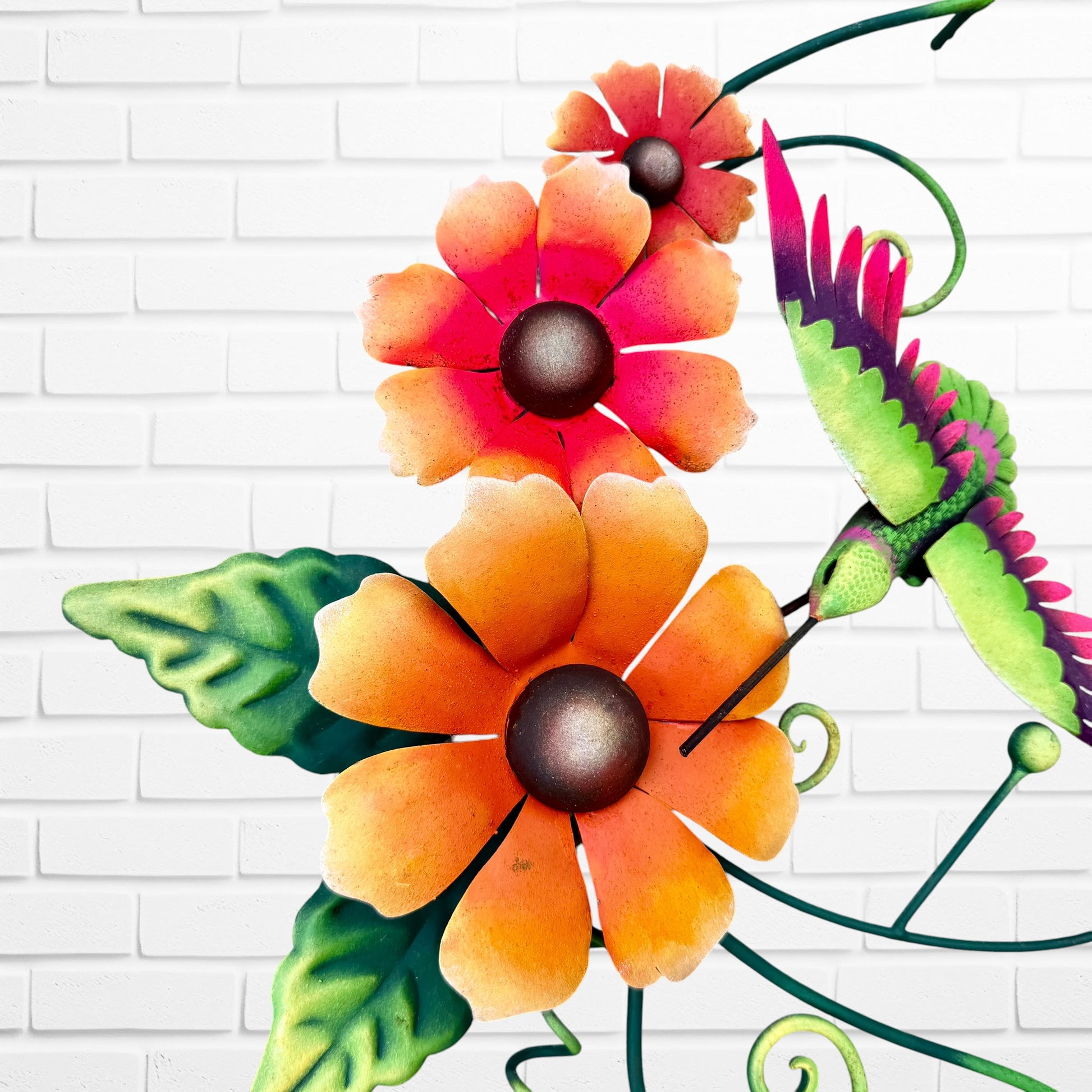 Decorative metal wall art with orange flowers and a hummingbird on a white brick background flower close up