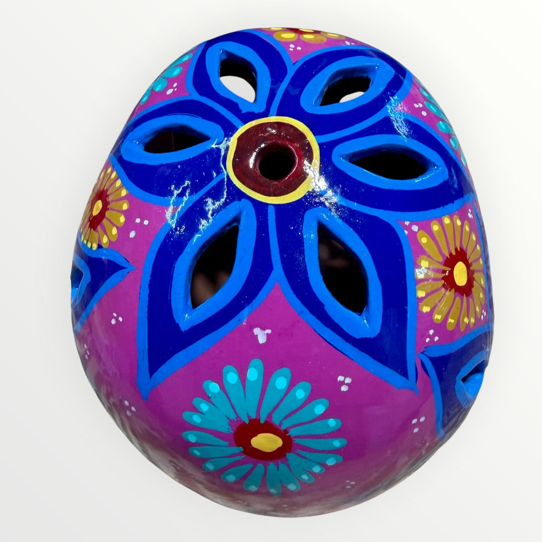 A hand-painted ceramic sugar skull mask in vibrant magenta pink, decorated with colorful floral and geometric patterns in blue, yellow, red, and white, set against a plain white background top of skull cut out view.