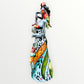 A Day of the Dead Catrina of a Frida skeleton doll holding a black cat, with a red parrot on her shoulder and colorful flowers around the top of her dress. Right side of doll showing a red parrot.