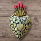 A Mexican Milagros medium heart in black with a gold and red flaming top, covered in antiqued golden charms. 