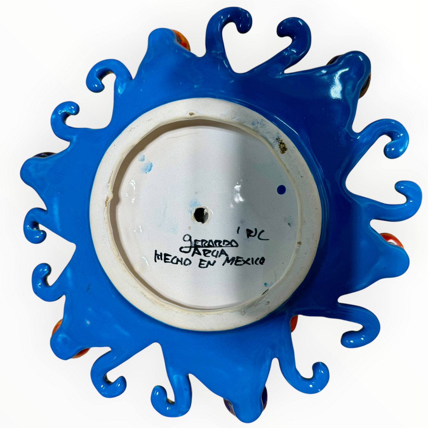 A colorful hand-painted Talavera ceramic sun wall decor piece with a smiling face, orange center, planets, and multicolored rays on a plain white background back view.