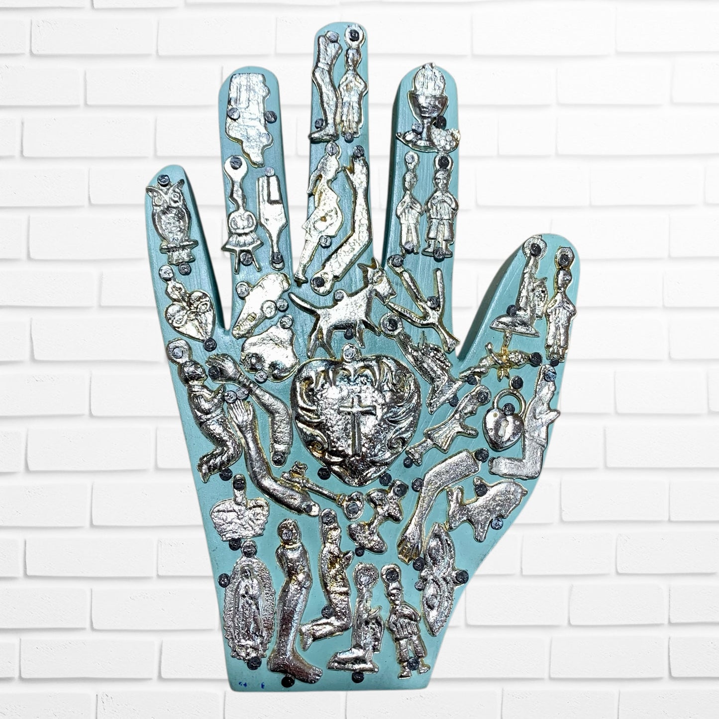 Decorative wall art of a hand with religious symbols on a white brick wall background blue