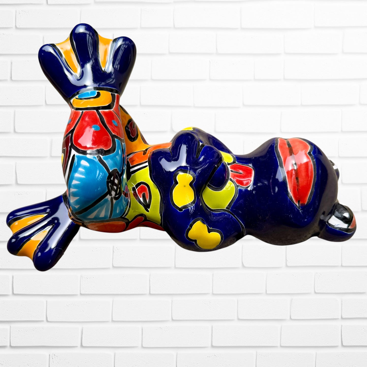 A colorful ceramic frog figurine sitting with arms crossed, decorated with vibrant hand-painted patterns in blue, yellow, red, orange, and light blue, set Left side view