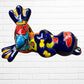A colorful ceramic frog figurine sitting with arms crossed, decorated with vibrant hand-painted patterns in blue, yellow, red, orange, and light blue, set Left side view